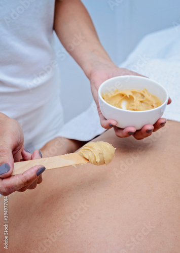 Spa therapist applying yellow scrub on young woman back.