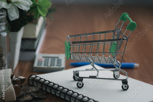 Green shopping cart, coin bag, Calculators, notebooks, and pens are all placed on a wooden table. photo