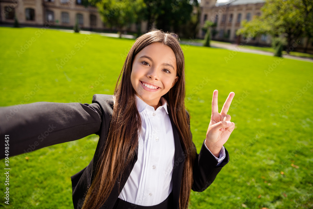 Photo of funny pupil girl make selfie showing v-sign look camera wear black uniform white shirt urban city outdoors Photo of funny pupil girl make selfie showing v-sign look camera wear black uniform white shirt urban city outdoors