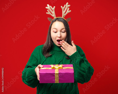 happy young woman with christmas deer antlers with gift on red background