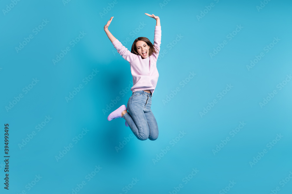 Full body photo of crazy excited girl jump enjoy childish free time raise hands wear lilac pullover isolated over blue pastel color background Full body photo of crazy excited girl jump enjoy childish free time raise hands wear lilac pullover isolated over blue pastel color background