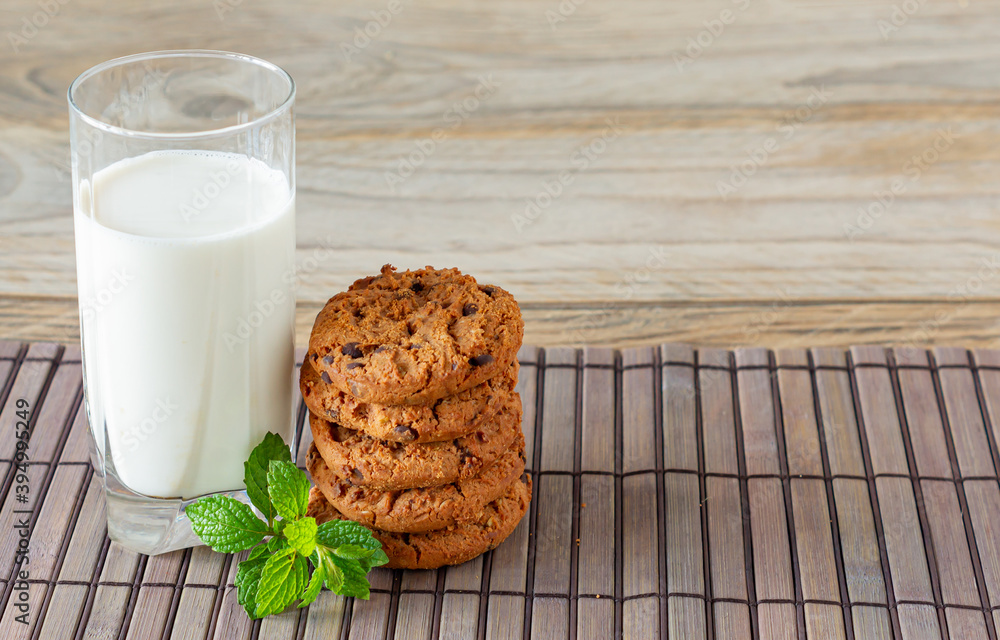 A stack of chocolate chips cookies on baking paper, with a glass of milk on a light wooden background A stack of chocolate chips cookies on baking paper, with a glass of milk on a light wooden background