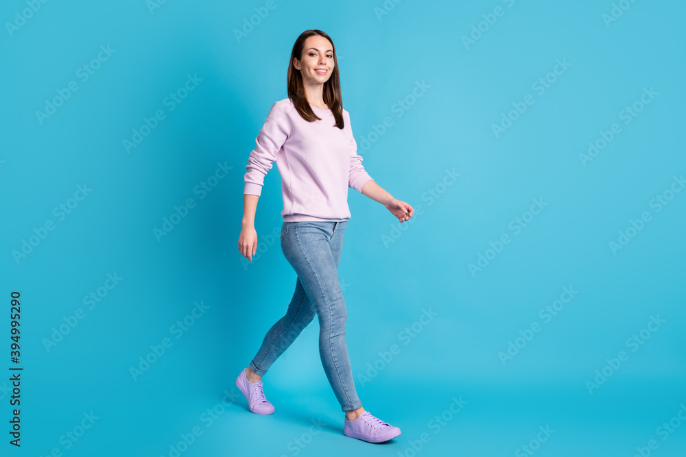 Full size profile photo of attractive lady hold good mood walk moving street season look positive wear casual purple sweatshirt pullover denim jeans footwear isolated blue color background Full size profile photo of attractive lady hold good mood walk moving street season look positive wear casual purple sweatshirt pullover denim jeans footwear isolated blue color background