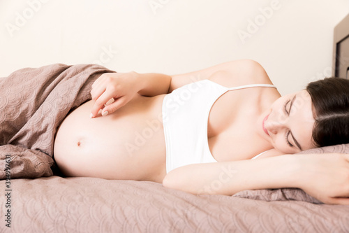 pregnant woman sitting in bed and touching her belly at home. pregnancy expectation concept