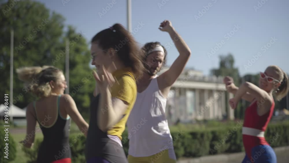 Young handsome 1980s man with retro tape recorder moving and singing as group of slim beautiful Caucasian women dancing around. Disco music and lifestyle concept. Young handsome 1980s man with retro tape recorder moving and singing as group of slim beautiful Caucasian women dancing around. Disco music and lifestyle concept.