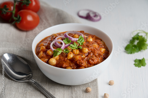 Chole masala also known as channay, chana is an indian street food made of chickpeas, chopped tomatoes, ghee and cumin decorated with red onion rings and parsley served in bowl with spoon on textile