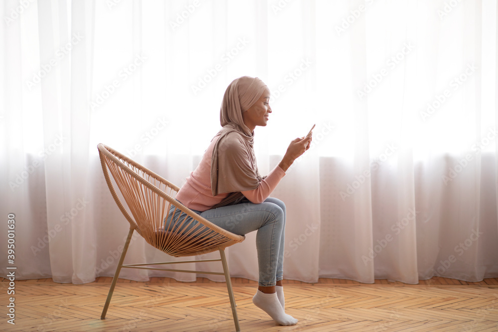 Young black Muslim woman in hijab using smartphone at home, working or studying online, copy space Young black Muslim woman in hijab using smartphone at home, working or studying online, copy space