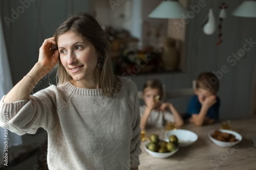 Girl in the kitchen looking to side, against the background of boys at table.