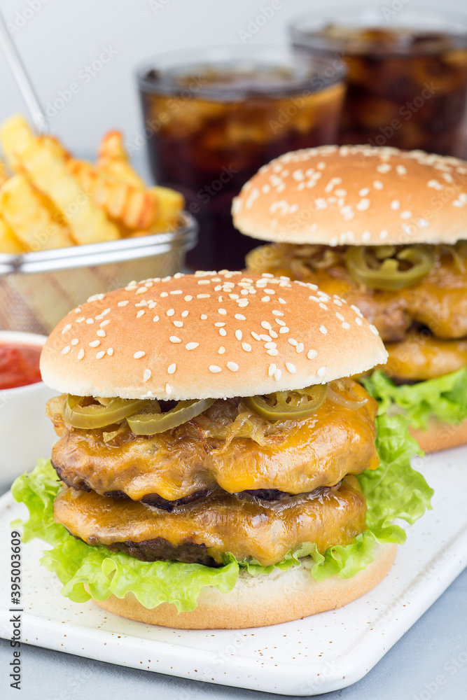 Homemade double cheese burger with two beef patty, cheddar cheese, lettuce, caramelized onion and jalapeno slices, served with french fries and soda, vertical