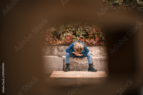 A cute little girl is sitting in sunglasses on a stone fence. Stylish child in a blue jacket. Casual style, fashion for children, fashionable suit, happy childhood © Дмитрий Ткачук