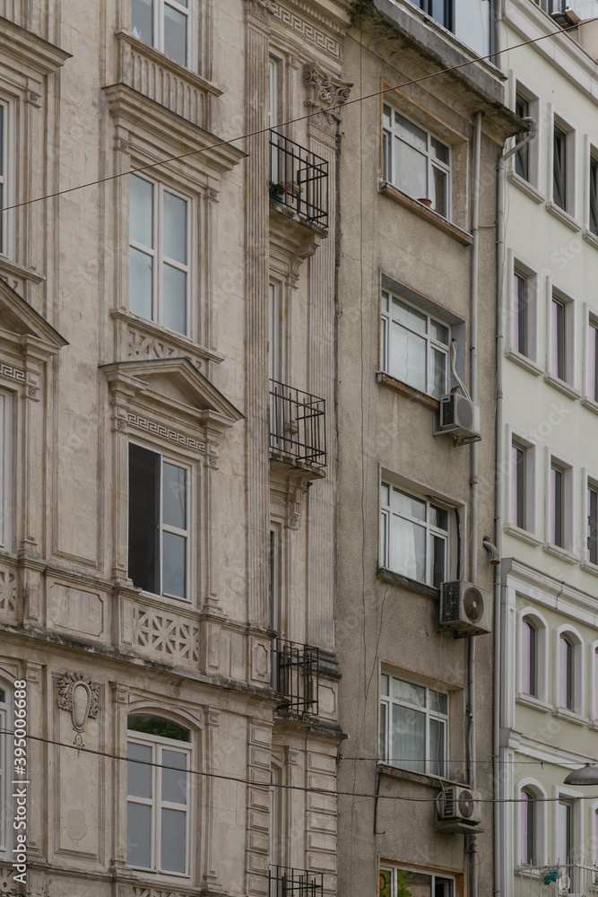 Old building facade with windows decorated with stucco frontones, false columns and balconies with wrought-iron bars. Vertical photo of a building with elements of city ​​communications.