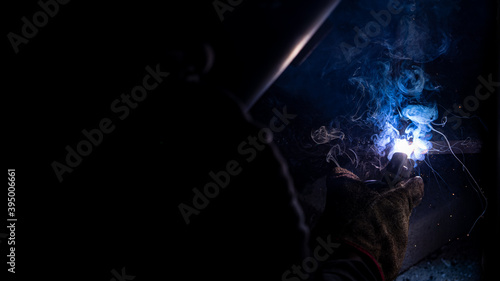 Homem trabalhando no escuro soldando ferro com ferramenta e fumaça