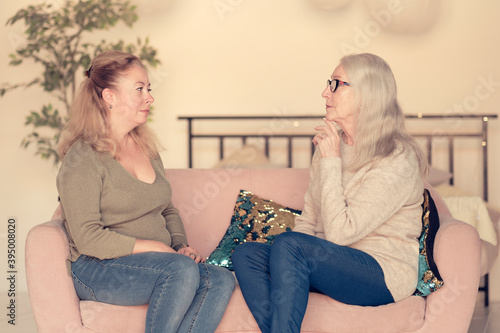 cute charming young female visiting her middle aged mother, sitting together on comfortable couch, having good conversation. Woman in her forties talking to daughter at home photo