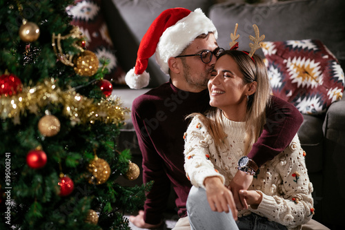 Young couple sitting on the floor near Christmas tree. Loving couple enjoy in holidays.