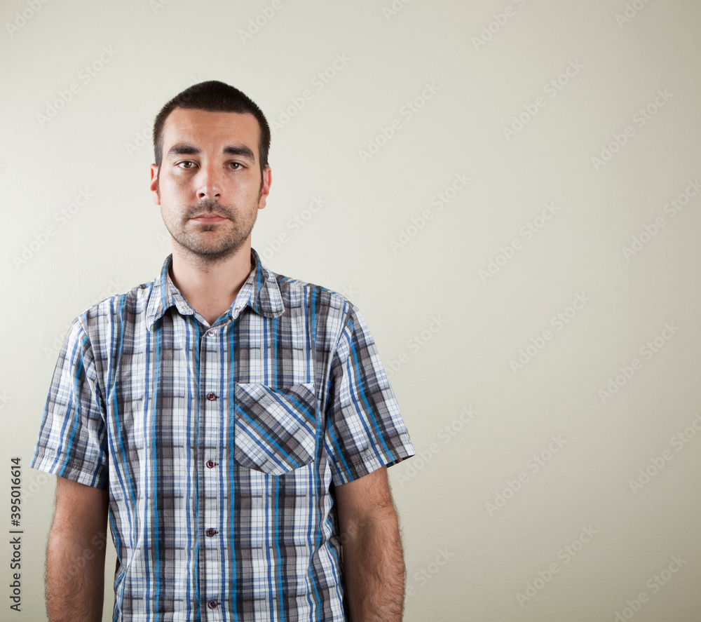 Obraz premium Studio photo of dark haired man with a short sleeved checkered shirt on a light brown beige background.