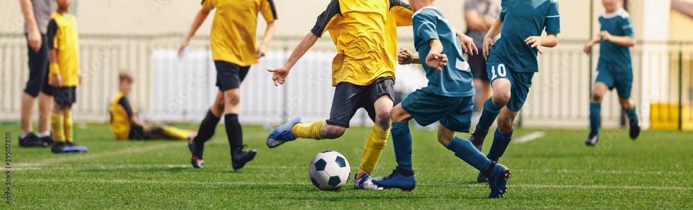 Horizontal image of football players kicking match. Boys in soccer duel. Kids in two football teams running after classic soccer ball. Horizontal sports background. Legs of young players on football Horizontal image of football players kicking match. Boys in soccer duel. Kids in two football teams running after classic soccer ball. Horizontal sports background. Legs of young players on football
