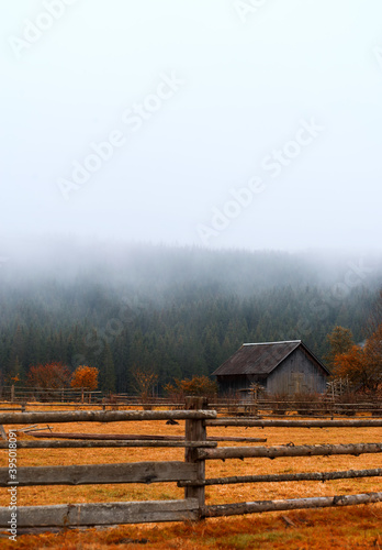 Beautiful autumn landscape of a wooden house in the mountains with foggy forest and orange grass