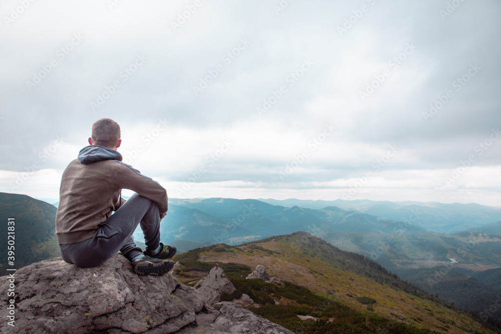 young strong man sitting on the rock at the top of the mountains peak