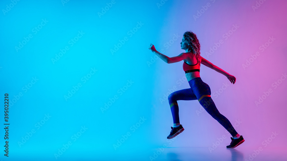 Runner. Young sportive woman training isolated on gradient blue-pink studio background in neon light. athletic and graceful. Modern sport, action, motion, youth concept. Beautiful female practicing.