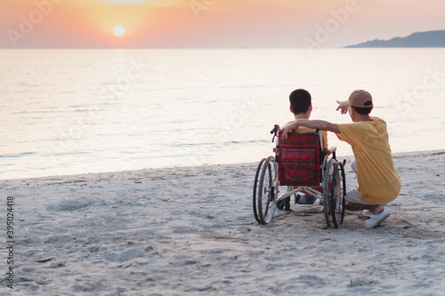 Father​ and Asian special child on wheelchair playing, doing activity on sea beach in summer, Lifestyle of disability child, Life in the education age, Happy disabled kid in travel holidays concept.