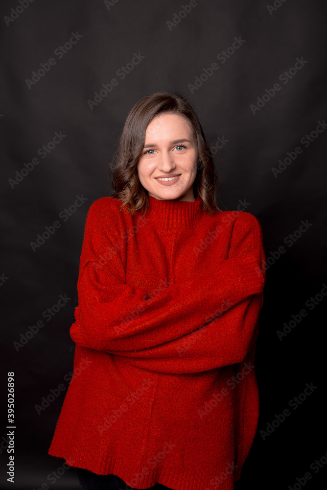 Portrait of young smiling girl in red sweater standing with arms folded and looking at camera over dark background Portrait of young smiling girl in red sweater standing with arms folded and looking at camera over dark background