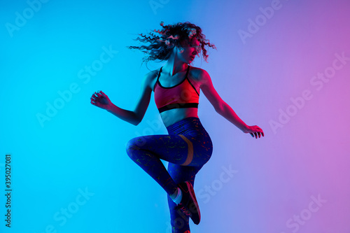 Sport dancing. Beautiful woman in bright sportwear isolated on gradient pink-blue background in neon light. Athletic and graceful. Modern sport, action, motion, youth concept. Female practicing