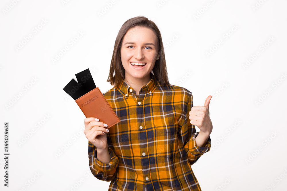 Smiling young traveler tourist woman posing showing thumb up hold passport tickets boarding pass isolated on white wall background studio portrait Smiling young traveler tourist woman posing showing thumb up hold passport tickets boarding pass isolated on white wall background studio portrait