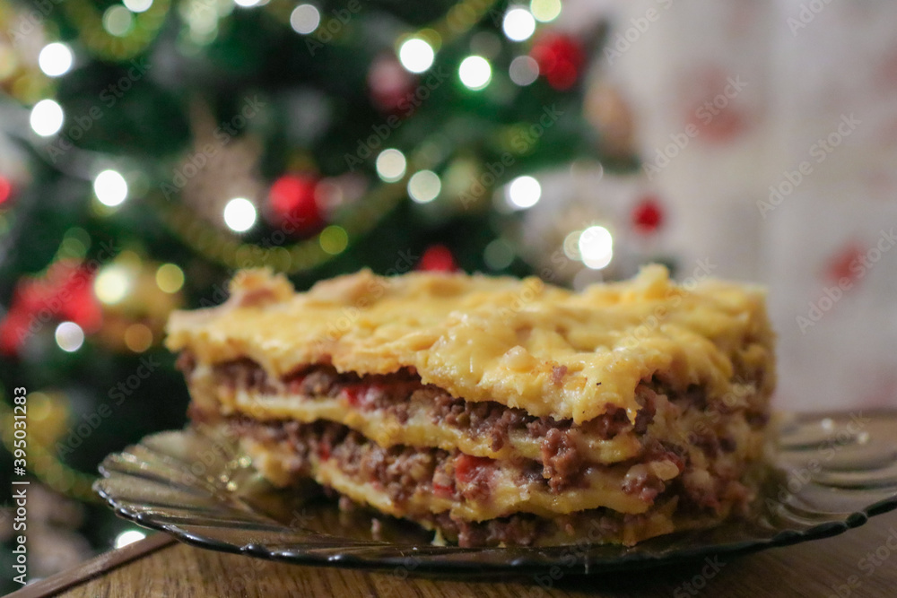 Festive lasagna stands on a wooden table. Delicious dish for the Christmas table. Christmas tree decorates the house. Holidays, holidays and winter. Festive lasagna stands on a wooden table. Delicious dish for the Christmas table. Christmas tree decorates the house. Holidays, holidays and winter.