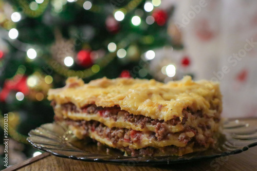 Festive lasagna stands on a wooden table. Delicious dish for the Christmas table. Christmas tree decorates the house. Holidays, holidays and winter.