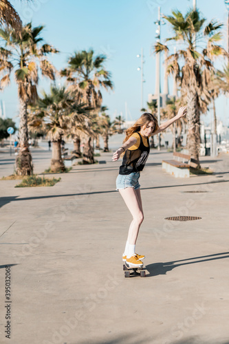 Skater girl riding a long board skate. Cool female urban sports. California style outfit. Woman on skateboard wearing pink glasses