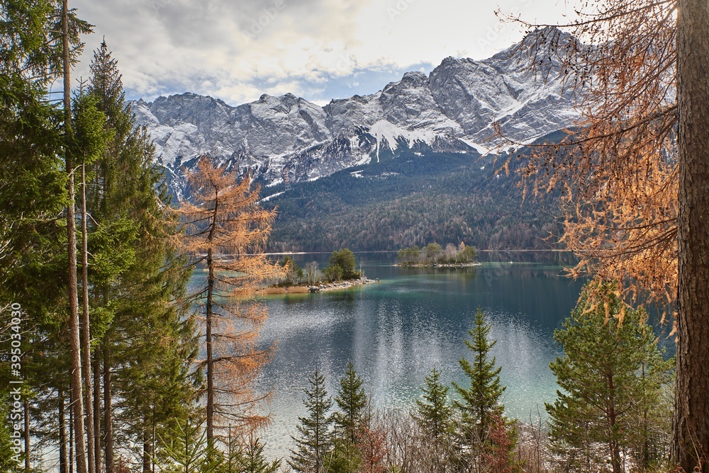 View of a reflecting mountain lake with colorful autumn trees in the foreground and snowy mountain peaks in the background.