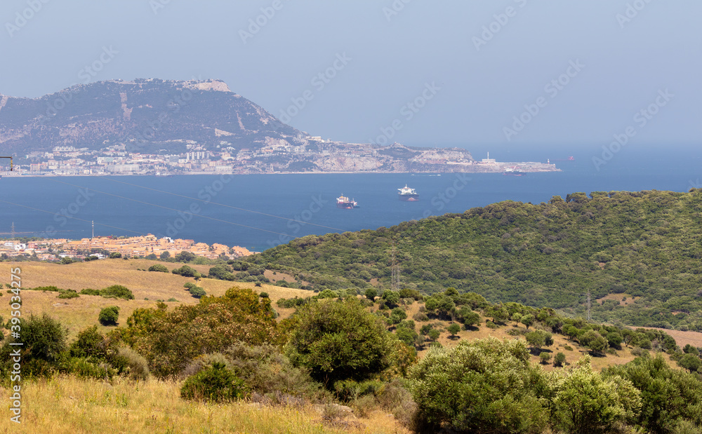 A distant view of the British peninsula Gibraltar from the Spanish coast. Ships are anchored in the bay. On the right you can see the lighthouse on a haze in summer.