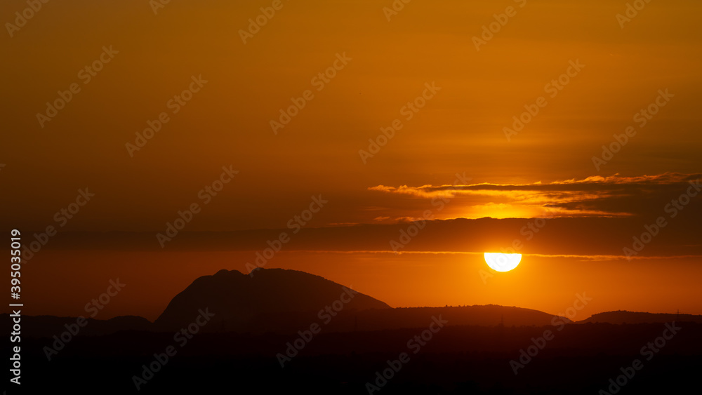 Silhouette of hills against beautiful golden hour sunset amidst a streak of clouds and beautiful orange sky
