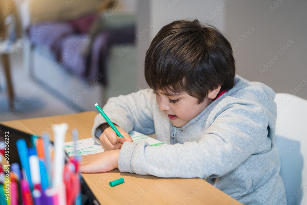 Candid shot happy kid sitting alone doing homework, Child boy with smiling face holding green pen drawing and colouring on white paper , Elementary school and homeschooling concept Candid shot happy kid sitting alone doing homework, Child boy with smiling face holding green pen drawing and colouring on white paper , Elementary school and homeschooling concept