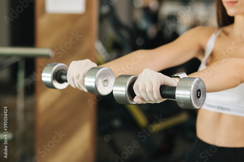Brunette woman in white gloves hold two dumbbells in hand. Female training in the gym