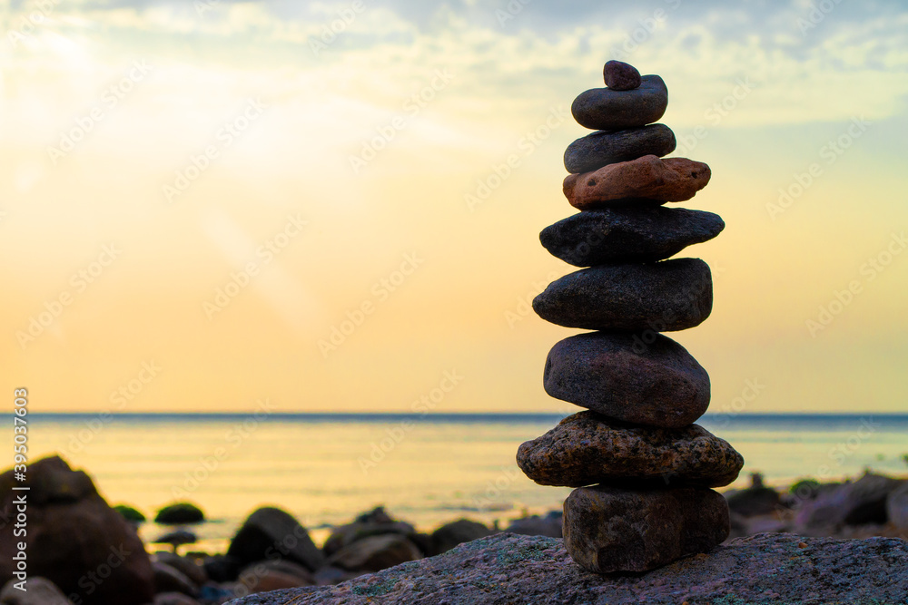 Fototapeta premium Stones pyramid on the seashore. Sunset on pebble beach. Balanced life, relax.