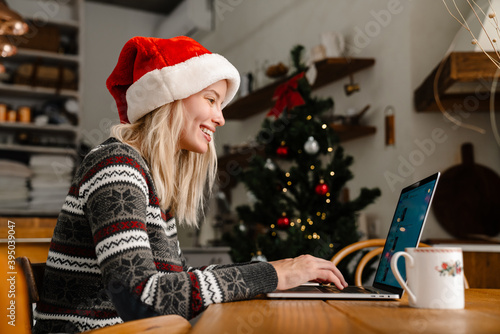 Happy nice girl in Santa Claus hat working with laptop and drinking tea