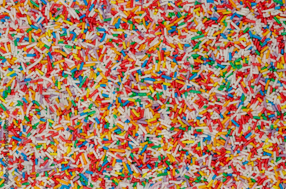 Rainbow sprinkles, background and surface. Rod-shaped colorful sugar sprinkles. Tiny candies in a variety of colors, used as decoration or topping. Backdrop. Food photo, top view, from above.