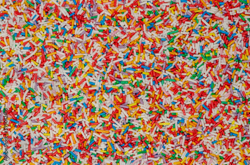 Rainbow sprinkles, background and surface. Rod-shaped colorful sugar sprinkles. Tiny candies in a variety of colors, used as decoration or topping. Backdrop. Food photo, top view, from above.