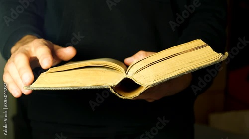 Hands turning old open antique book pages, moving through old literature. Man skimming through a simple retro, vintage thick book, reading concept. Bible, prayer book, dictionary, novel
