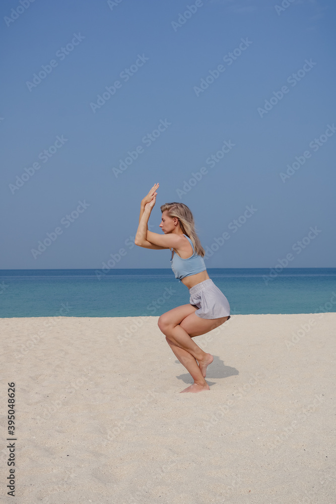 Blonde young girl practices yoga and meditation in the Garudasana, eagle pose asana on the beach on a sunny day. Blonde young girl practices yoga and meditation in the Garudasana, eagle pose asana on the beach on a sunny day.