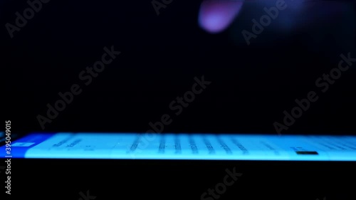 Man browsing the internet on his smartphone in a dark room. Finger hovering over a bright mobile phone screen, tapping it Side view, macro, extreme closeup Surfing the web on mobile device in darkness