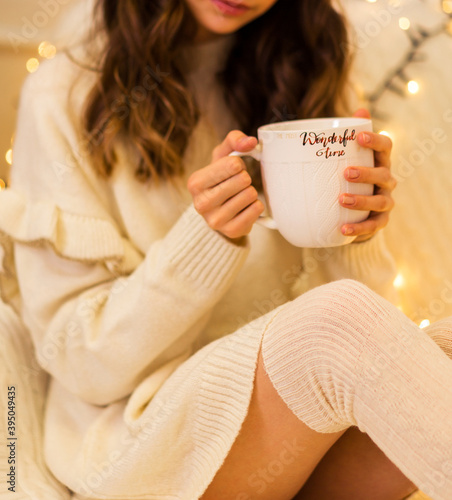 A girl in a white sweater and leggings holds a large white cup in her hands
