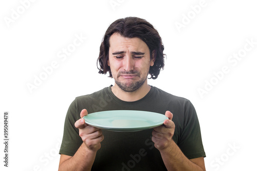 Desperate man crying as looks at an empty dish plate in his hands, isolated on white background. Dissatisfied guy weeping as has no food to eat. Global crisis and hunger issue. Famine and starvation