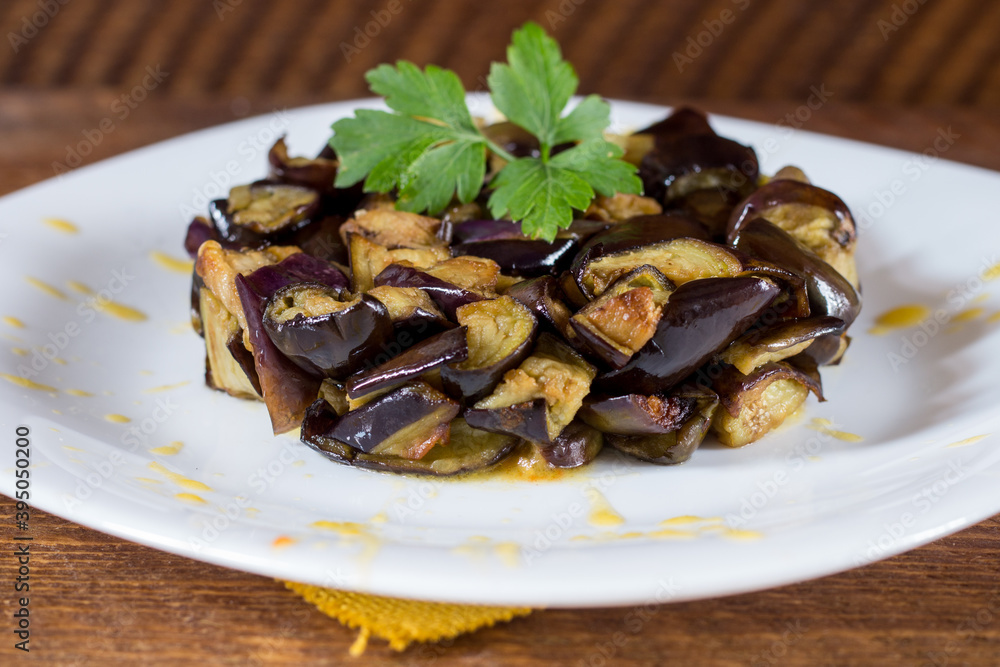 Plate of diced aubergines on a cream of yellow cherry tomatoes in a white plate. Wood background. Selective focus. Plate of diced aubergines on a cream of yellow cherry tomatoes in a white plate. Wood background. Selective focus.