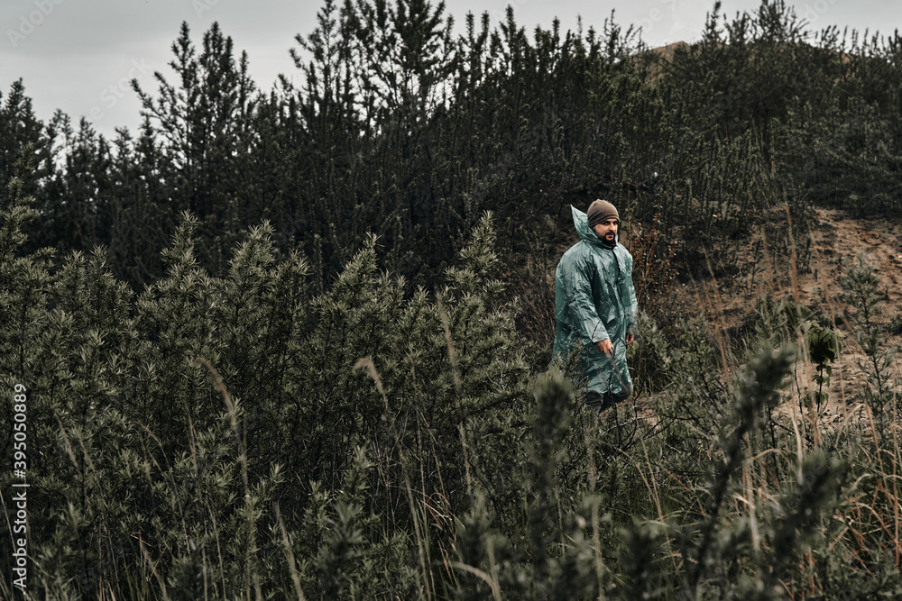 A man in a green raincoat walks along a country road, cloudy, autumn.