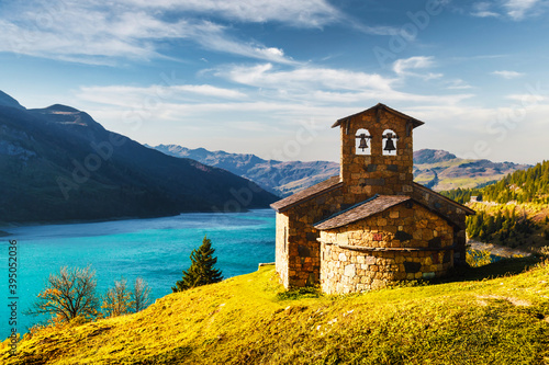 Sunny picturesque view of stone chapel on Roselend lake (Lac de Roselend) in France Alps (Auvergne-Rhone-Alpes). Landscape photography