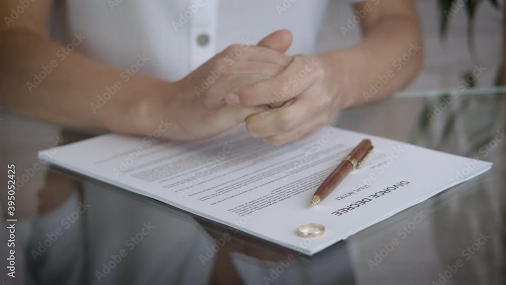 Divorce decree on the table. A view of a stressed woman's hand and a wadding ring on the table with divorce papers. Divorce decree on the table. A view of a stressed woman's hand and a wadding ring on the table with divorce papers.