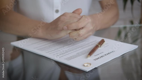 Divorce decree on the table. A view of a stressed woman's hand and a wadding ring on the table with divorce papers. photo