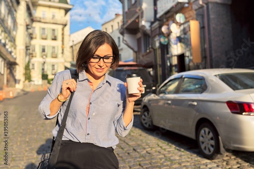 Mature business woman in glasses with office laptop bag walking along city street